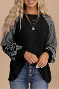 Woman wearing a black top with patterned sleeves and blue jeans on a beige background