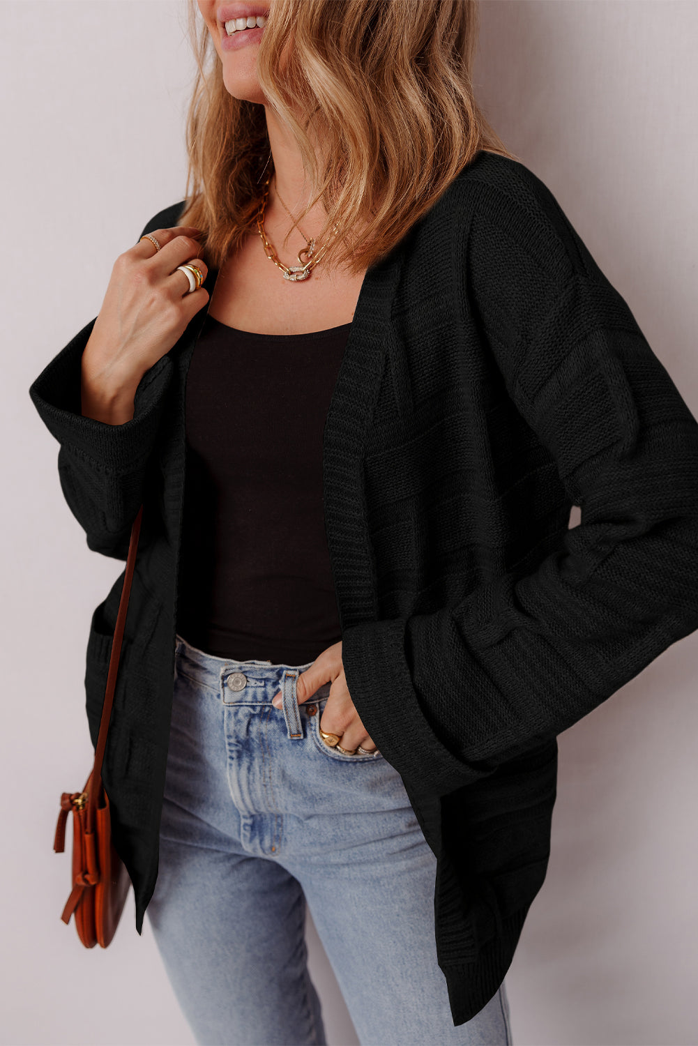 Woman wearing a black cardigan, black top, and light blue jeans against a plain background
