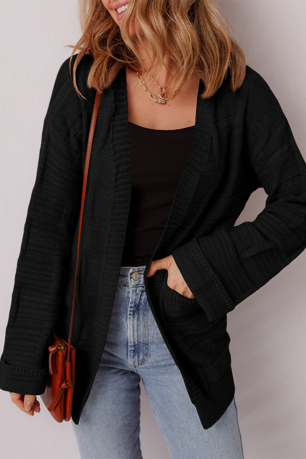 Person wearing a black cardigan, black top, and light blue jeans with a brown leather bag.