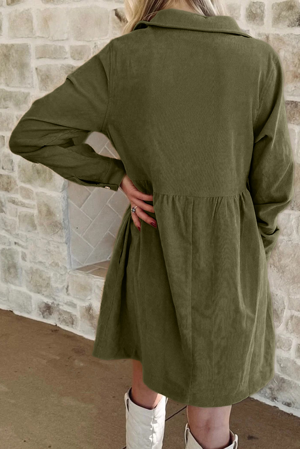 Person wearing an olive green dress against a brick wall.