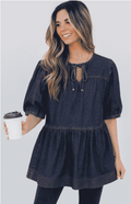 Woman wearing a denim dress holding a coffee cup against a plain background