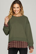 Woman wearing a green sweatshirt with plaid cuffs and hem on a gray background