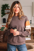 Woman wearing a brown sweatshirt with color-block sleeves, holding a coffee cup indoors.