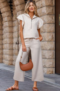 Woman in a white outfit with a brown handbag standing against a stone wall.