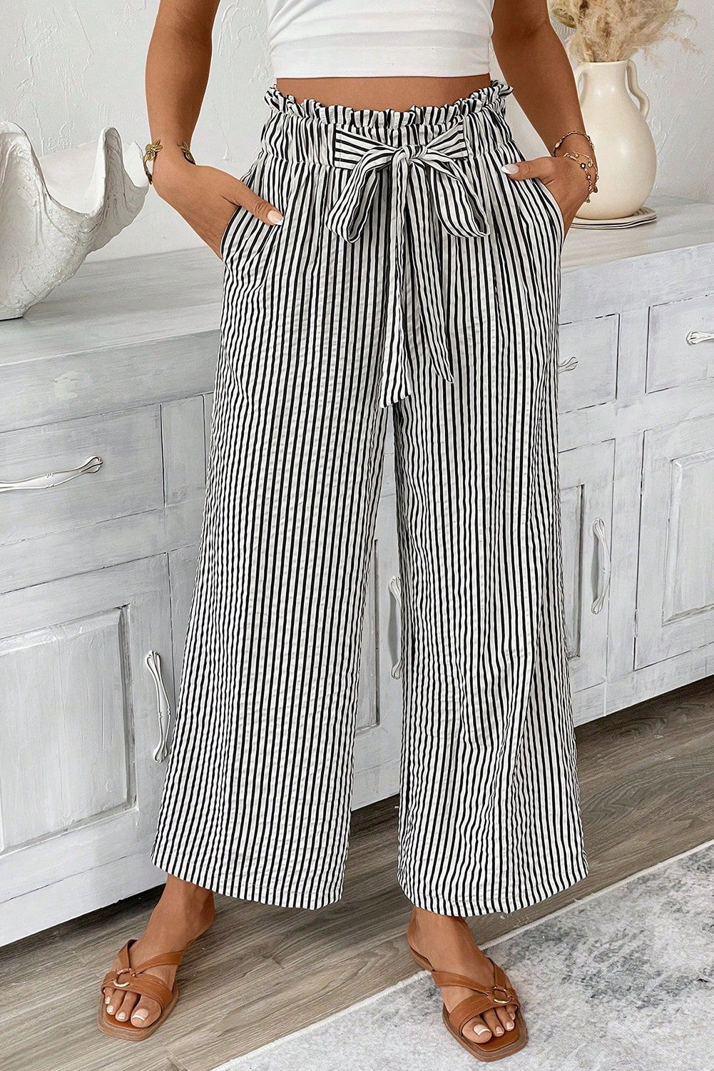 Person wearing black and white striped wide-leg pants with a white top in a bathroom setting.